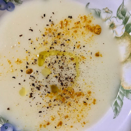 Fotografía de una crema creada con ingredientes vegetales de color blanco: calabaza vieira, patatas y nabo; decorada con cúrcuma, pimienta negra y aceite de oliva virgen extra.