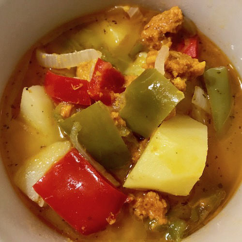 Fotografía de un guiso de patatas con pimientos, rojo y verde, embutido de calabaza y pimentón.